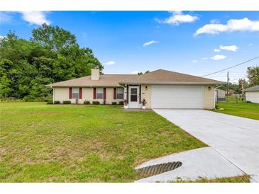 Inviting single-story home featuring a well-manicured lawn and neutral exterior with red shutters and a two-car garage at 12 Hemlock Radial Pass, Ocala, FL 34472