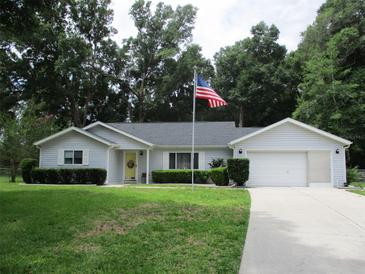 Charming single-story home with manicured lawn, attached garage, and a US flag on display at 14192 Sw 112Th Cir, Dunnellon, FL 34432