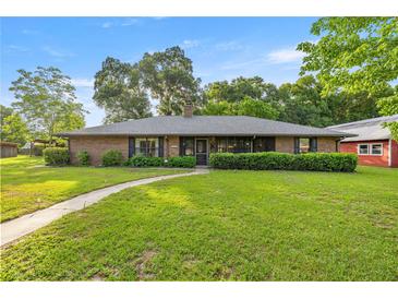 Charming brick home featuring a lush front lawn, mature trees, and a welcoming walkway leading to the front door at 6497 W Anthony Rd, Ocala, FL 34479