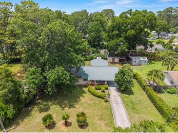 An aerial view of a single-story home that features a long driveway and lush landscaping, including large trees and manicured bushes at 3621 Se 12Th Pl, Ocala, FL 34471