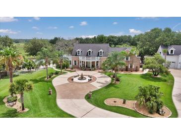 Stunning brick home featuring manicured lawn, circular drive with fountain, and lush tropical landscaping at 4550 County Road 104, Oxford, FL 34484