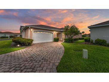 Charming home featuring a brick driveway, attached garage, manicured lawn, and beautiful landscaping at 8670 Se 141St Pl, Summerfield, FL 34491