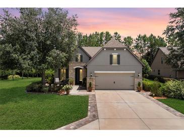 Charming home exterior boasts a two-car garage, stone accents, and a lush green lawn at sunset at 9158 Sw 65Th Loop, Ocala, FL 34481