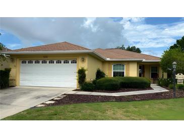 Charming single-story home with a well-manicured lawn, a two-car garage, and yellow paint at 9490 Sw 94Th Ct, Ocala, FL 34481