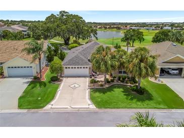 Beautiful home with a well-manicured lawn, mature landscaping, and a view of the golf course and lake at 1266 James Island St, The Villages, FL 32162