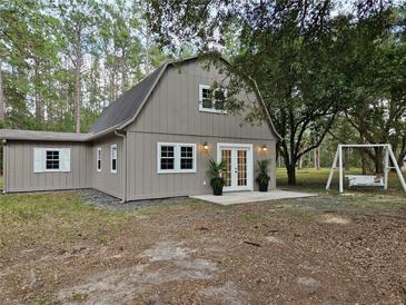 Charming gambrel house with double doors, white trim, front patio, and complemented by lush greenery and a swing at 9805 Se 182Nd Avenue Rd, Ocklawaha, FL 32179