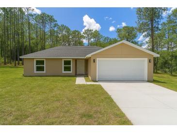 Charming single-story home featuring a two-car garage, a well-maintained lawn, and a tree-lined backdrop at 391 Nw Crocus Ln, Dunnellon, FL 34431