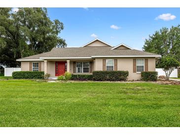 Charming single-story home featuring well-manicured lawn, lush landscaping, and inviting red front door at 4360 Se 106Th St, Belleview, FL 34420