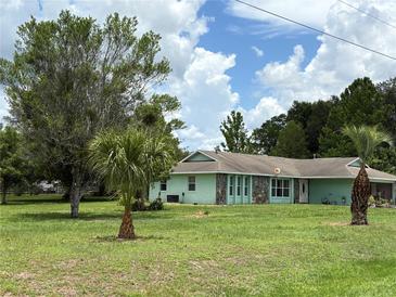 Charming single-story home with light green paint and stone accents sits on a lush green lawn with mature trees at 6773 Se 87Th St, Ocala, FL 34472