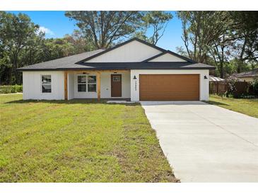 Charming single-story home featuring a well-manicured lawn, attached garage, and welcoming front porch at 13803 Se 44Th Ave, Summerfield, FL 34491
