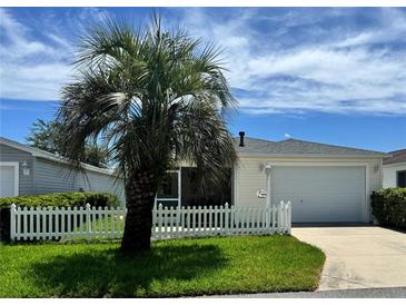Charming single-story home featuring a well-manicured lawn, a white picket fence, and a mature palm tree at 889 Allagash Ave, The Villages, FL 32162