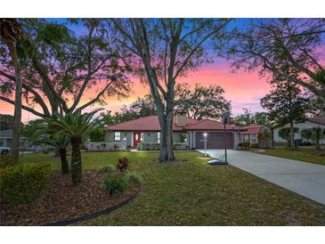 Charming home with a red-tiled roof, manicured lawn, mature trees, and inviting sunset sky at 128 Lake Ring Dr, Winter Haven, FL 33884