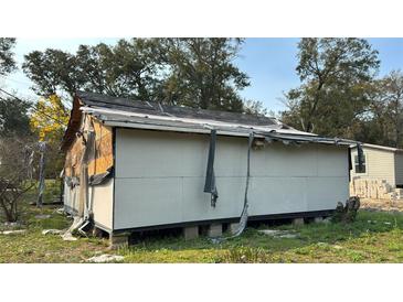 Damaged exterior of unfinished home with partial siding and roof repairs evident in rural setting at 1928 Old Apopka Rd, Apopka, FL 32703