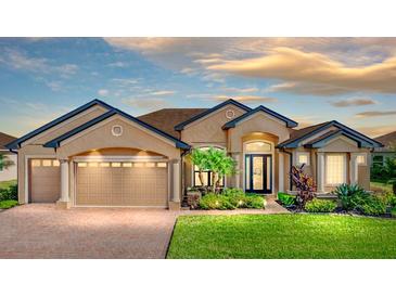 Charming tan home features a three-car garage, beautiful landscaping, brick driveway and walkway at 1336 Oakmont Dr, Winter Haven, FL 33884