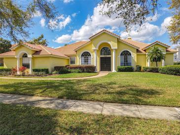 Beautiful yellow home featuring a well-manicured lawn, lush landscaping, and a tile roof at 2204 Kettle Dr, Orlando, FL 32835