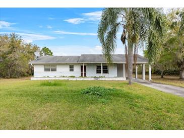 Charming single-story home featuring a covered carport, a well-manicured lawn and mature trees at 6261 Red Grange Blvd, Indian Lake Estates, FL 33855