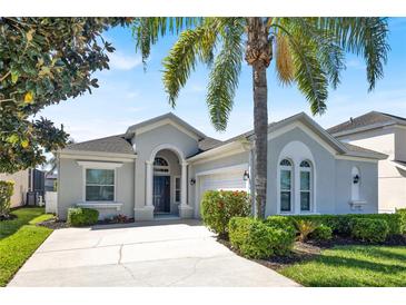 Charming single-story home featuring a stucco exterior, a two-car garage, manicured landscaping, and a welcoming arched entryway at 908 Orista Dr, Davenport, FL 33897