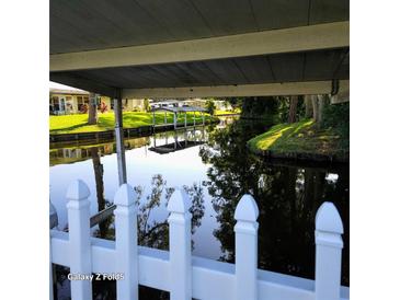 A serene canal view with boat dock is seen from under a covered patio and through a white picket fence at 167 Bonnie Dr, Auburndale, FL 33823