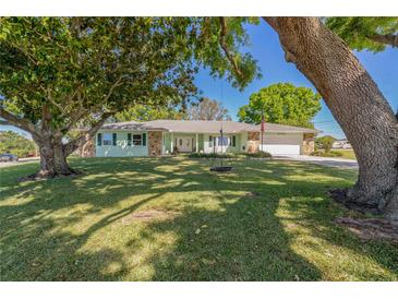 Charming single-story home with a lush front yard and mature trees providing shade on a sunny day at 6754 Winterset Gardens Rd, Winter Haven, FL 33884