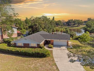 Charming single-story brick home boasts a well-manicured lawn, long driveway, and scenic sunset backdrop at 102 Lake Ring Dr, Winter Haven, FL 33884