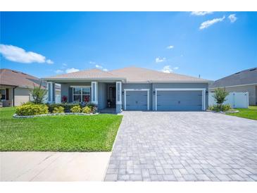 Charming single-story home with a well-manicured lawn, paver driveway, and a two-car garage under a clear blue sky at 157 Walkers Point Dr, Auburndale, FL 33823