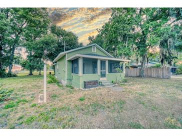 Charming, light-green cottage-style home with a screened-in porch, surrounded by mature trees and a cloudy sky at 230 Denton Ave, Auburndale, FL 33823