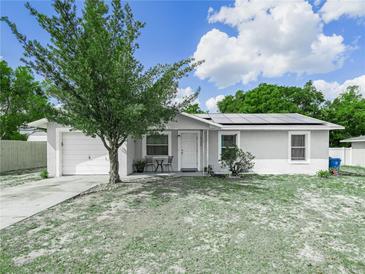 Charming single-story home with a well-manicured lawn, mature tree, and solar panels on the roof at 2100 Magnolia Ave, Haines City, FL 33844