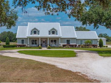 Charming single-story home features a metal roof, lovely front porch, circular driveway, and beautifully manicured landscaping at 3805 Mammoth Grove Rd, Lake Wales, FL 33898