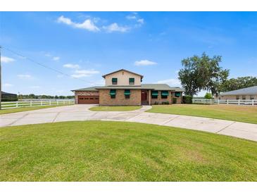 Charming two-story home with brick facade, lush lawn, circular driveway, and green awnings provides curb appeal at 2731 State Road 557, Lake Alfred, FL 33850