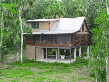 Stunning log home on piers, featuring a screened porch and a metal roof, surrounded by lush greenery at 2530 Arbuckle Shores Rd, Frostproof, FL 33843