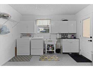 Bright laundry room features modern washer and dryer, ample cabinet storage, and convenient utility sink at 1411 Juarez Pl, The Villages, FL 32159