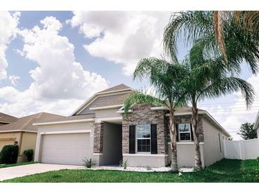 Charming single-story home with stone accents, lush lawn, and beautiful palm trees at 414 Taft Dr, Davenport, FL 33837