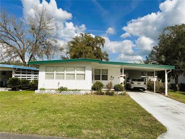 Charming single-story home with a carport, landscaped yard, and white picket fence under a beautiful blue sky at 115 Camellia Trl, Leesburg, FL 34748