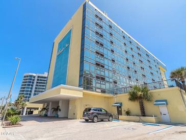 Stunning exterior view of a yellow oceanfront condominium under a bright blue sky at 1909 S Atlantic Ave # 703, Daytona Beach, FL 32118
