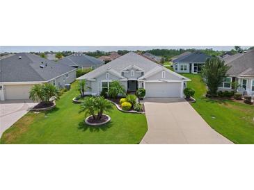 Landscaped front yard featuring lush lawn, decorative trees and shrubbery leading to a gray home with a two car garage at 924 Figwood Loop, The Villages, FL 32163