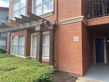 Exterior view of a stucco condo featuring a pergola and manicured landscaping near the unit entrance at 5108 Conroy Rd # 1713, Orlando, FL 32811