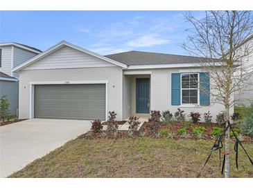 Charming single-story home featuring a grey garage door, blue door, manicured landscaping, and vibrant plants at 5410 Catmint Dr, Lake Hamilton, FL 33851