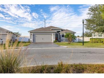 Single-story home with gray exterior, paver driveway, and landscaped lawn at 113 Promenade Ct, Auburndale, FL 33823
