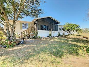 Tan mobile home with large screened porch, wooden steps, and a spacious yard at 301 Evandee Ct, Kissimmee, FL 34758