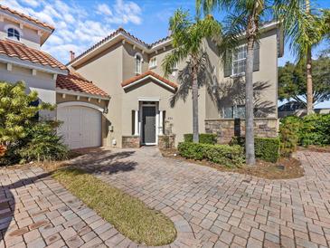 Tan two-story home with tile roof, paver driveway, and lush landscaping at 220 Brunello Dr, Davenport, FL 33897
