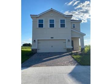 Two-story house with a beige exterior, two-car garage, and paved driveway at 1144 Trappers Trail Loop, Davenport, FL 33896