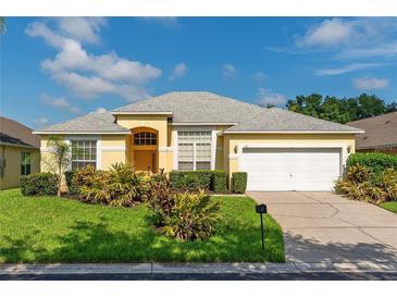 Beautiful yellow house with a gray roof, white garage door, and lush landscaping at 135 Langham Dr, Davenport, FL 33897