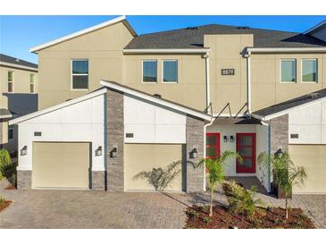 Tan three-story townhome with two-car garage, red door, and landscaping at 8879 Cabot Cliffs Dr # 103, Davenport, FL 33896