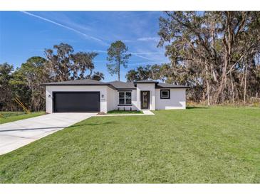 White house with gray garage door and landscaping; spacious lawn at 13142 Sw 43Rd Avenue Rd, Ocala, FL 34473