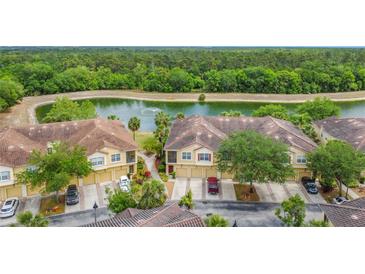 Aerial view of townhomes with tile roofs situated on a pond and surrounded by mature trees at 2833 Oakwater Dr # 169, Kissimmee, FL 34747