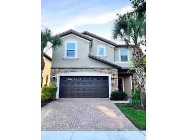 Two-story house with dark brown garage door, brick driveway, and palm trees at 2112 Morocco Way, Kissimmee, FL 34747