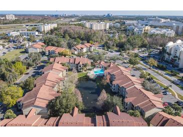 Stunning aerial view of community featuring tile roofs, mature trees, and a sparkling blue community pool with pond at 3004 Parkway Blvd # 202, Kissimmee, FL 34747