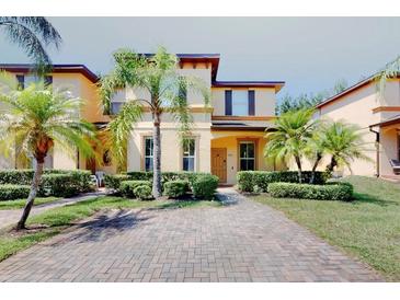 Inviting two-story townhome featuring a brick driveway and well-manicured landscaping with mature palm trees at 3939 Calabria Ave, Davenport, FL 33897