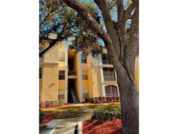 Bright yellow condominium building with mature shade trees and well-maintained landscaping at 8813 Dunes Ct # 7 201, Kissimmee, FL 34747