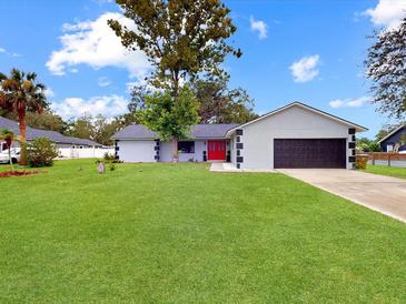 Charming single-story home featuring a manicured lawn, red front door, and attached two-car garage at 1710 Big Oak Ln, Kissimmee, FL 34746